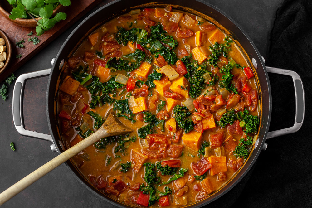 best African peanut soup in large black pot with sweet potatoes, kale and tomatoes