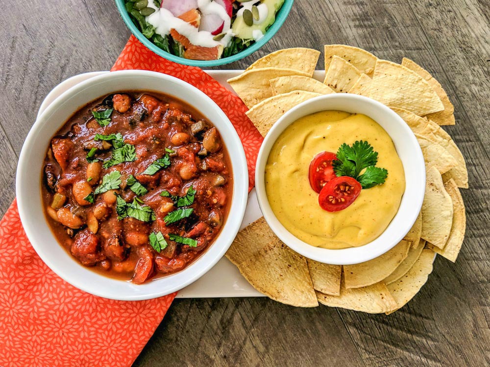 Fire-roasted Mushroom Plant Based Pinto Chili with Chili Lime Salad Tortilla Chips and Nacho Sauce