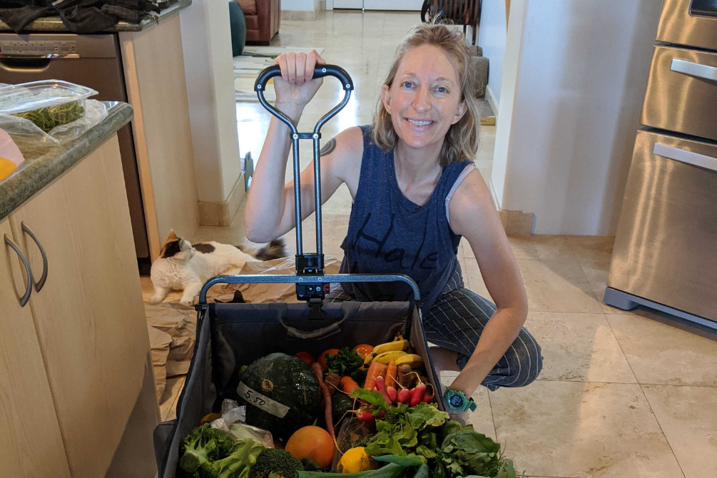 Ways to save on groceries while vegan or plant based. The picture is of our co-founder, Molly, with a wagon full of produce from the farmer's market.